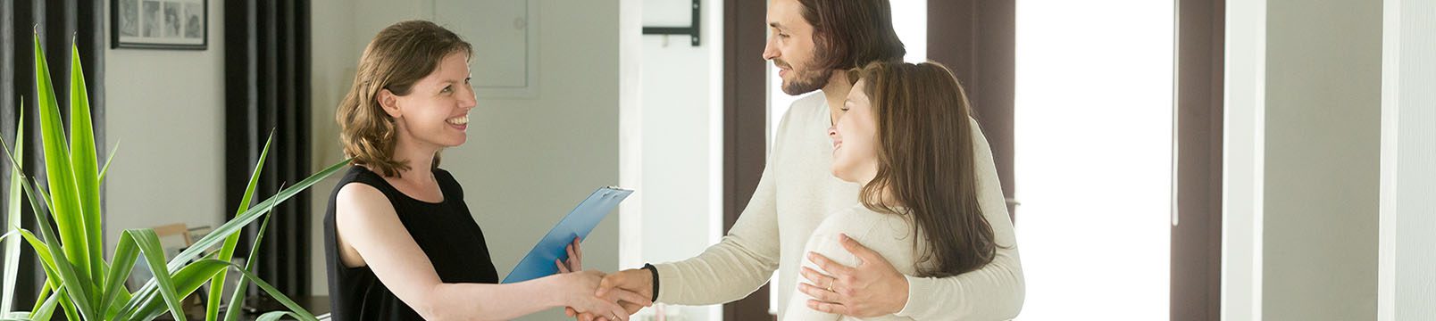friendly woman shaking hands with couple in bright house